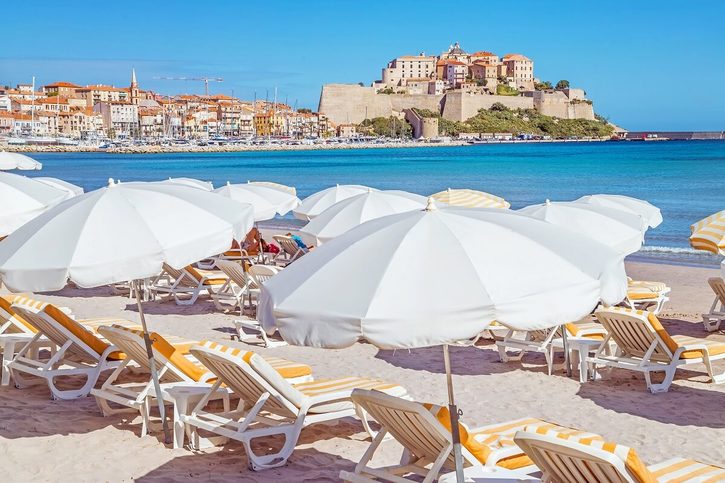 Calvi - Písečná pláž s tyrkysovým mořem a výhledem na historickou citadelu.